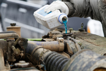 An auto mechanic pours antifreeze into the radiator of an old car engine. Shallow focus.