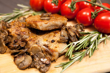 Close up image on pork steak on wooden board next to grilled mushrooms and cherry tomatoes