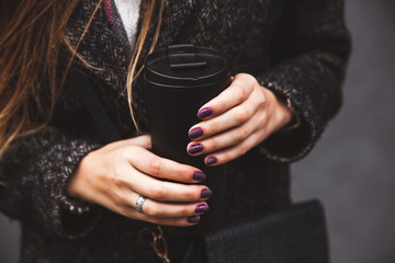 girl in stylish coat with beautiful manicure hand holding a black vacuum tumbler on a gray background