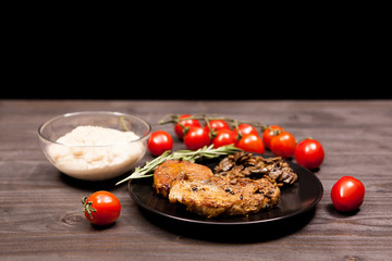 Roasted Pork steak in black plate with grilled mushrooms, oregano cherry tomatoes and bean paste on a wooden table