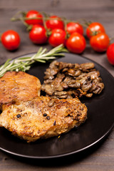 Roasted pork in black plate with grilled mushrooms, oregano cherry tomatoes and bean paste on a wooden table
