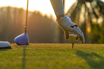 Fotobehang Golf Hand aziatische vrouw golfbal op tee zetten met club in golfbaan op avond en zonsondergang tijd a voor gezonde sport. Levensstijlconcept.