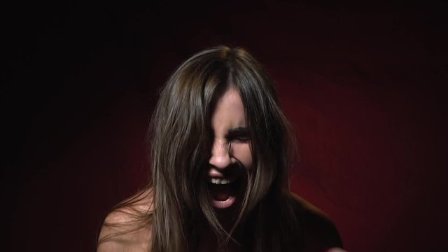 A woman with disheveled hair screams with anger, slow motion
