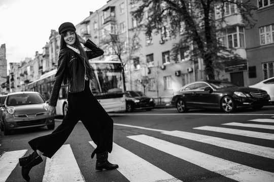 Beautiful girl with sunglasses. A model in a stylish wide-brimmed hat at a pedestrian crossing. Harmoniously similar clothes in gray tones. Street style shooting. Women's fashion.