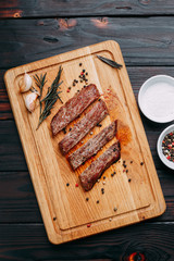 Appetizing meat. Grilled well-done beef steak with with herbs and spices on cutting board, flat lay. Restaurant menu concept