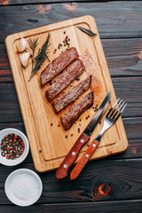 Grilled beef steak with herbs and spices on cutting board and cutlery. Top view with copy space
