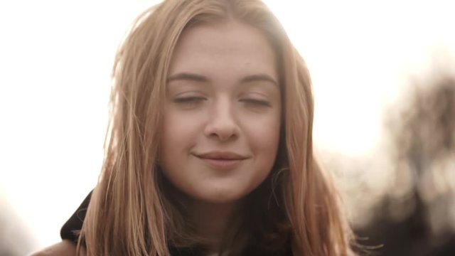 Closeup portrait of beautiful female having natural makeup looking on camera and smiling while wind blowing her light brown hair in slow motion. Cinematic look