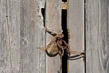 Verrostetes, altes Vorhängeschloss an einer verwitterten Holztür.