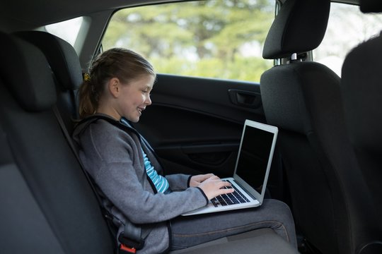 Teenage girl using laptop in the back seat