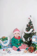 Boy in Christmas Elf costume. A baby near a Christmas tree.