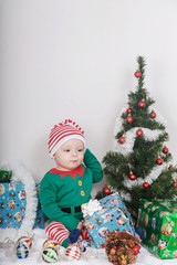 Boy in Christmas Elf costume. A baby near a Christmas tree.