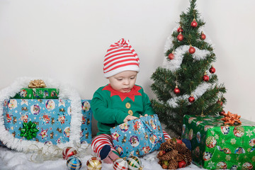 Boy in Christmas Elf costume. A baby near a Christmas tree.
