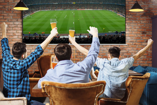 Group of young men cheering on their favorite football team watching the game on TV at the local pub having beer.