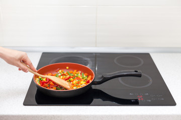 Vegetables are in a frying pan. Woman cooking colourful fresh vegetables on an electric stove