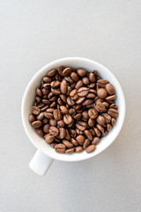 White cup with coffee beans on gray woden background