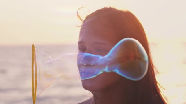 Young happy brunette woman blowing soap bubbles on the beach at beautiful sunset and smiles in slow motion by the sea. 1920x1080