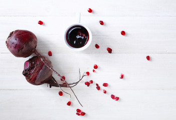 beet, pomegranate seeds and Cup with beet juice on white wooden table