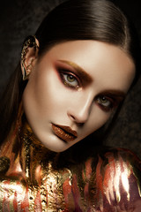 Gold Woman skin. Beauty fashion model girl with Golden make up.Hairstyle and make up