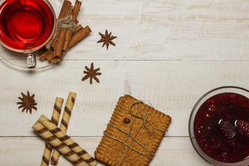 Tea in a cup with raspberry jam, cookies, croissants, cinnamon, anise, caramel sticks. On a white wooden table. Christmas composition. View from above.