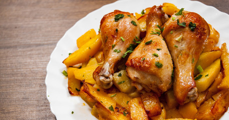 grilled chicken leg and potatoes on the white plate on a wooden background.