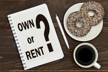 Notebook with a notes OWN or RENT on the office table with coffee and donuts . Concept BUY or RENT