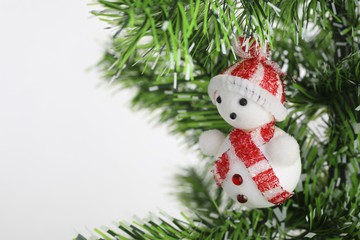 small toy snowman dressed in striped red and white cap and scarf sitting on Christmas tree