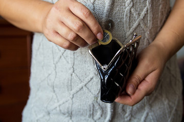 The woman holds the coins over the old empty wallet. The concept of poverty