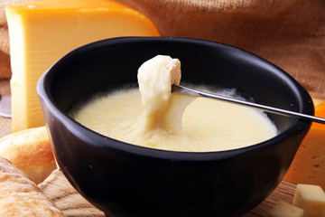 Gourmet Swiss fondue dinner on a winter evening with assorted cheeses on a board alongside a heated pot of cheese fondue with two forks dipping bread and white wine behind in a tavern or restaurant