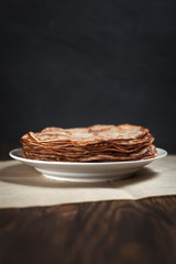 pancakes stacked in a plate on a dark wooden table on a dark gray background