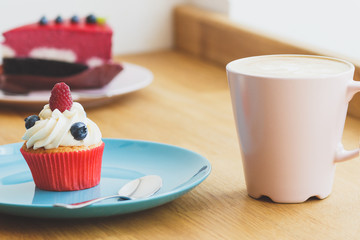 Small cupcake with raspberry and blueberry on the plate, cup of hot cappuccino