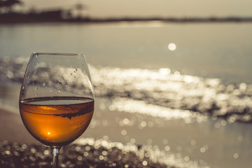Glass of wine on sand on sea background.