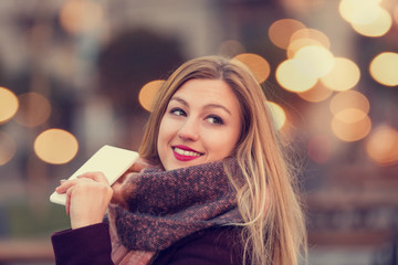 Beautiful attractive smiling woman holding cellphone. Bokeh concept.