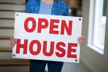 Woman standing in the living room holding open sign 