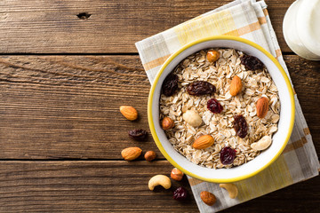 Oat flakes with nuts and dried fruits in bowl on dark wooden table