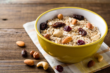 Oat flakes with nuts and dried fruits in bowl on dark wooden table