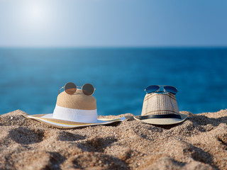 Pair of sunglasses and sunhats on the beach sand against the sea.
