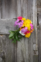 Bouquet of bright summer flowers on rough weathered wooden wall background.