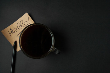 Morning strong coffee and a note with the inscription "Hello" on a black background with space for text. Flat lay.