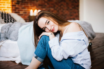 Obraz premium Красивая молодая девушка с длинными волосами смотрит в камеру сидя на полу в комнате Beautiful young girl with long hair looking at camera sitting on the floor in the room