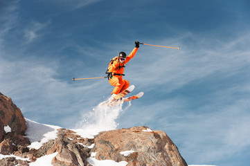 An athlete skier is jumping from high rock high in the mountains.