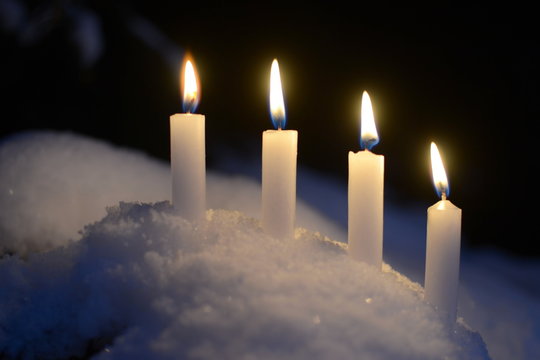 Four white burning candles outdoors in the snow