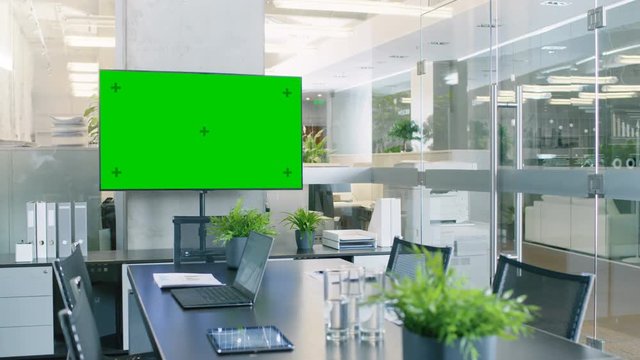 Modern Empty Meeting Room with Big Conference Table with Various Documents and Laptops on it, on the Wall Big TV with Green Chroma Key Screen. RED EPIC-W 8K Camera.