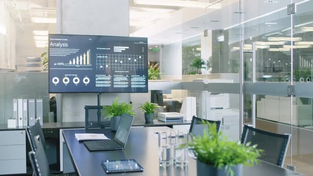 Modern Empty Meeting Room with Big Conference Table with Various Documents and Laptops on it, on the Wall Big TV Showing Company's Growth, Statistics and Pie Charts. RED EPIC-W 8K Camera.