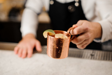 Bartender in white shirt and apron holding a cup with a fresh ginger drink