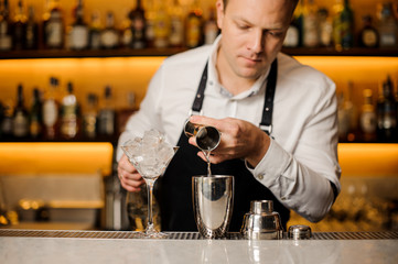 Barman pouring a portion of alcoholic drink into the shaker