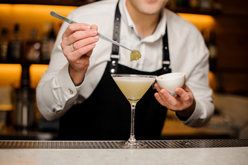 Barman in white shirt and apron decorating a cocktail with a birch leaf