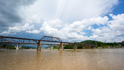 a bridge with cloudy sky and brown river - obrazy, fototapety, plakaty