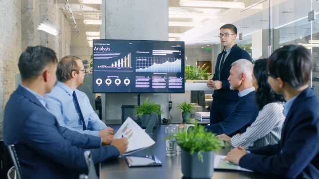 Talented Young Analyst Gives Report/ Presentation to Business Executives, Showing Company's Growth on the Wall TV. Shot on RED EPIC-W 8K Helium Cinema Camera.