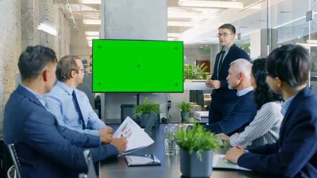 Businessman Gives Report/ Presentation to His Business Colleagues, Pointing at Green Chroma Key Screen Wall TV. Shot on RED EPIC-W 8K Helium Cinema Camera.