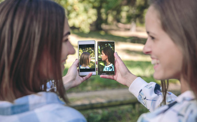 Happy women showing smartphones with their side view portraits photos taked over a forest background